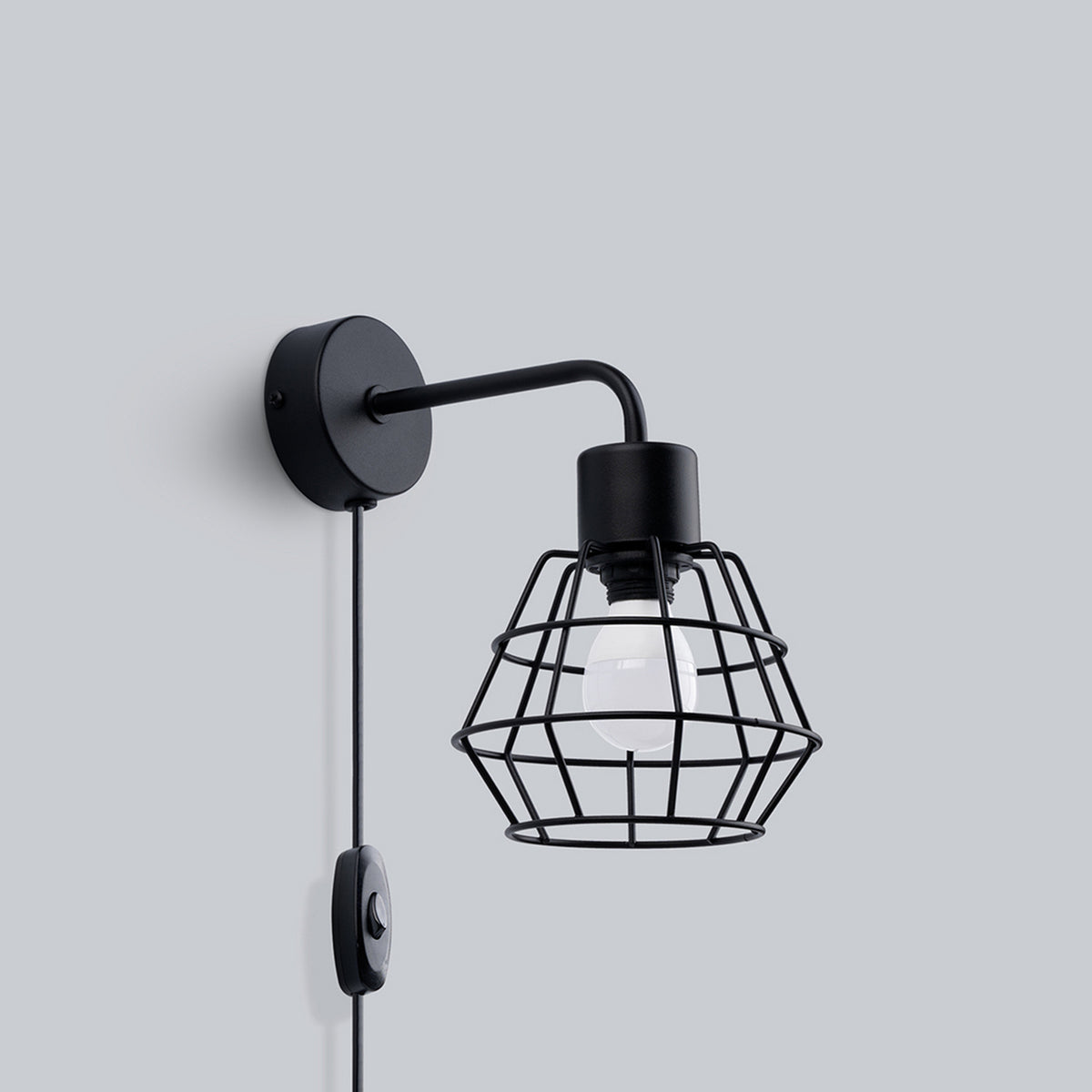 Vue de trois quarts de l'applique noire fixée sur un mur gris clair.