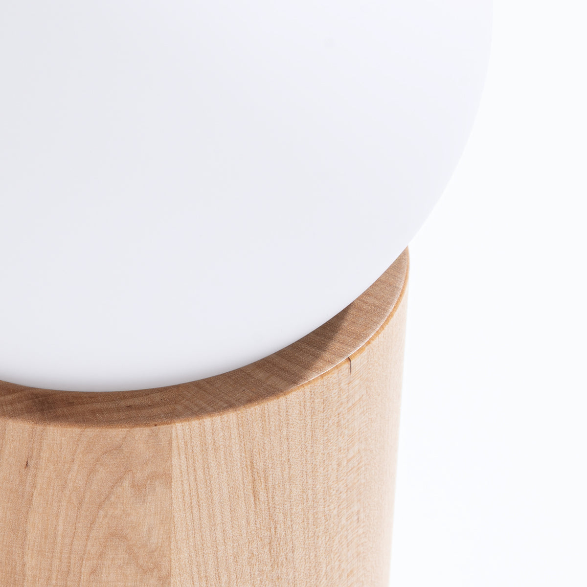 Gros plan sur la jonction entre le globe blanc et le socle cylindrique en bois.