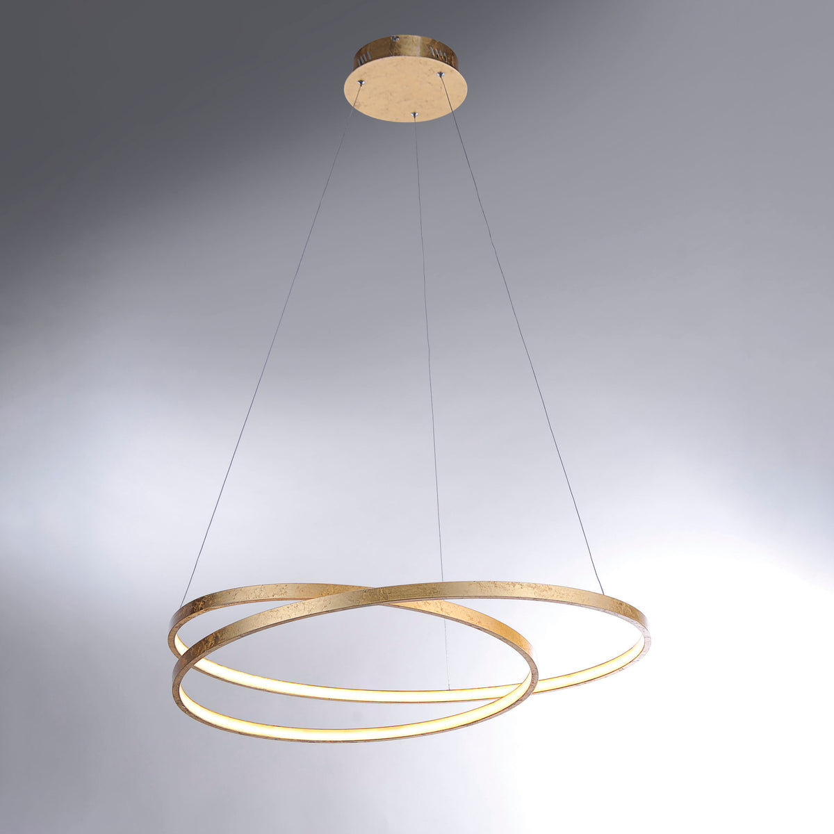 Vue rapprochée du luminaire doré montrant les anneaux superposés et la lumière chaude.