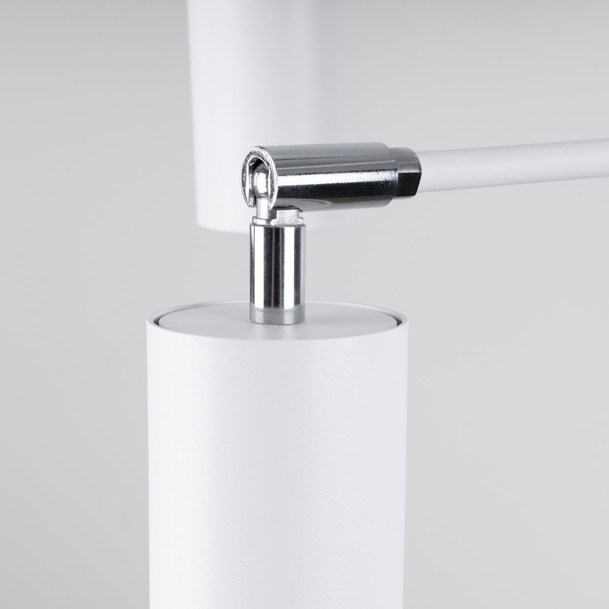 Gros plan sur l'articulation chromée entre le bras blanc et le cylindre orientable du luminaire.