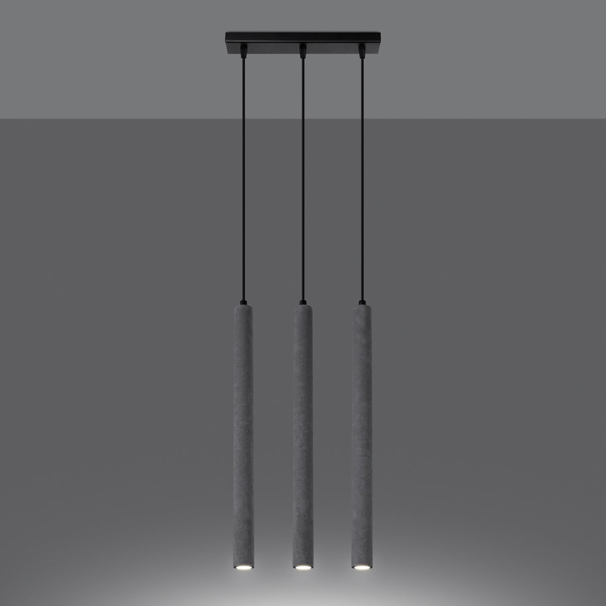 Luminaire suspendu allumé dans une ambiance sombre, trois cylindres diffusant une lumière vers le bas.