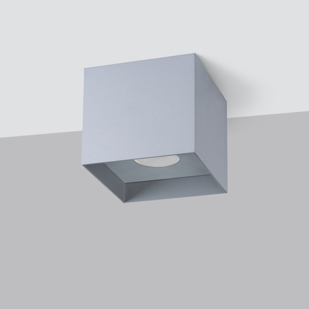 Plafonnier gris carré installé au plafond, montrant sa fixation et son volume.