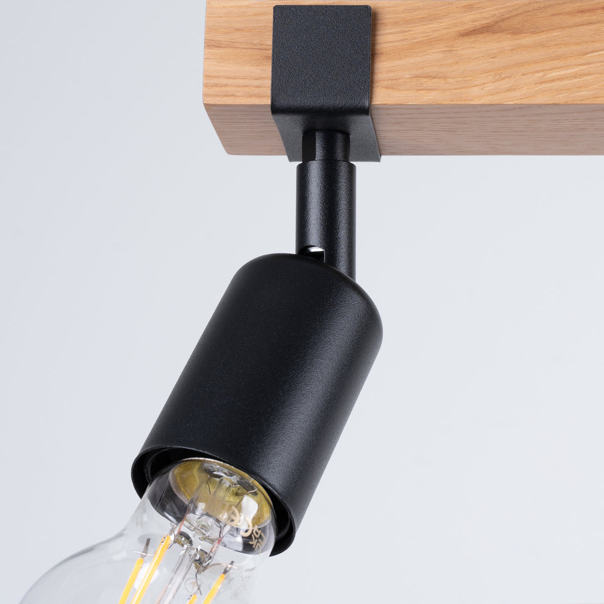 Détail de la finition : spot noir articulé fixé sur la barre en bois clair.