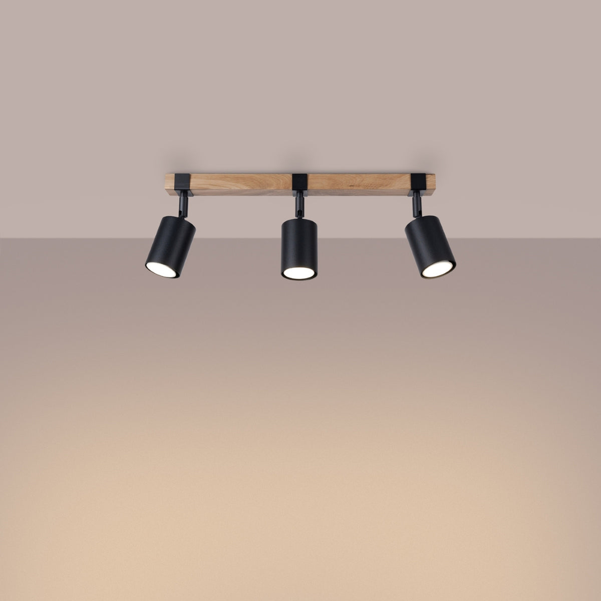 Luminaire installé au plafond, éclairant un mur beige, spots orientés vers le bas.