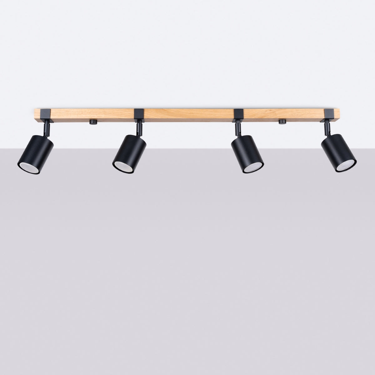 Vue de face sur fond gris du luminaire quatre spots noirs et support en bois.