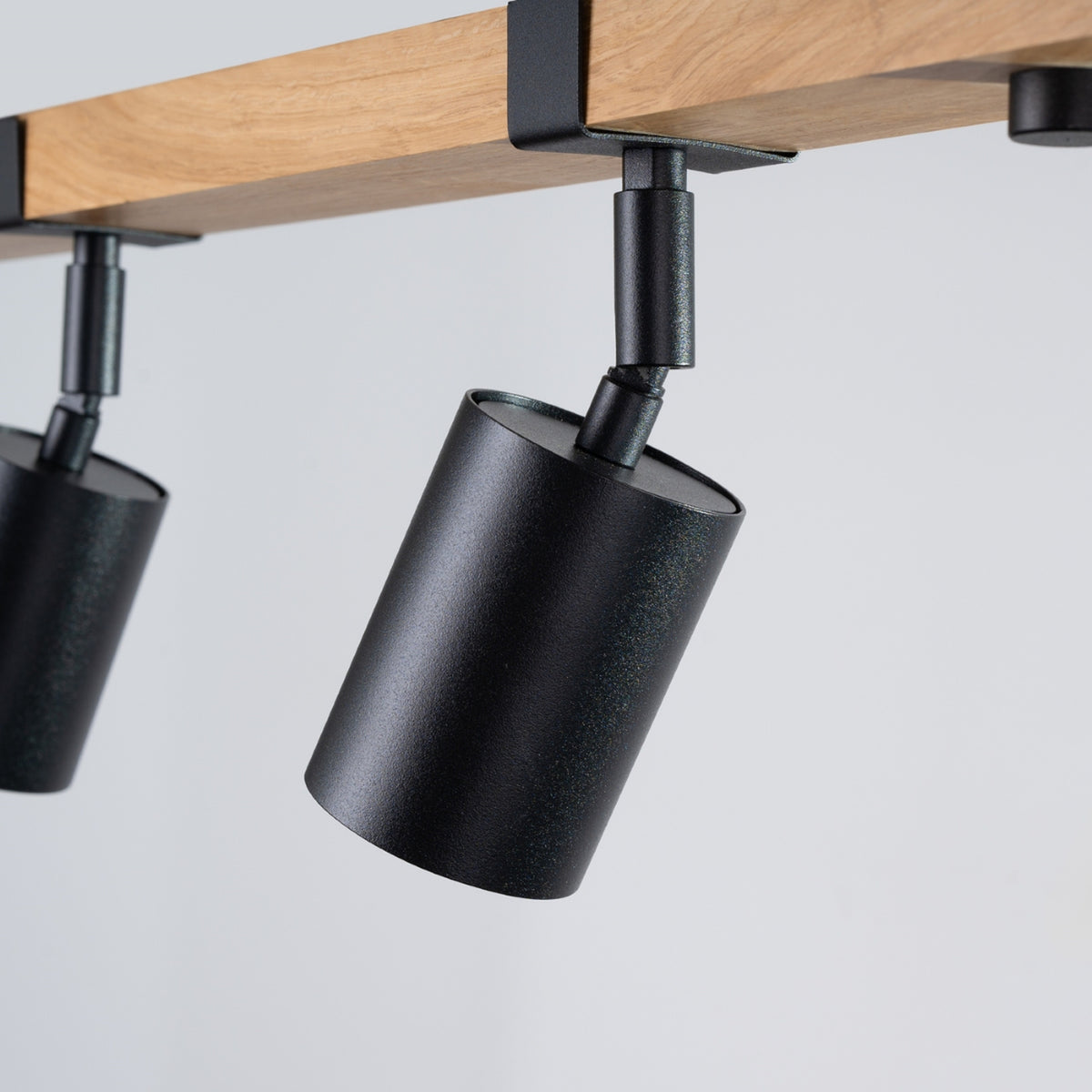 Gros plan sur un projecteur cylindrique noir texturé et son support métallique articulé.
