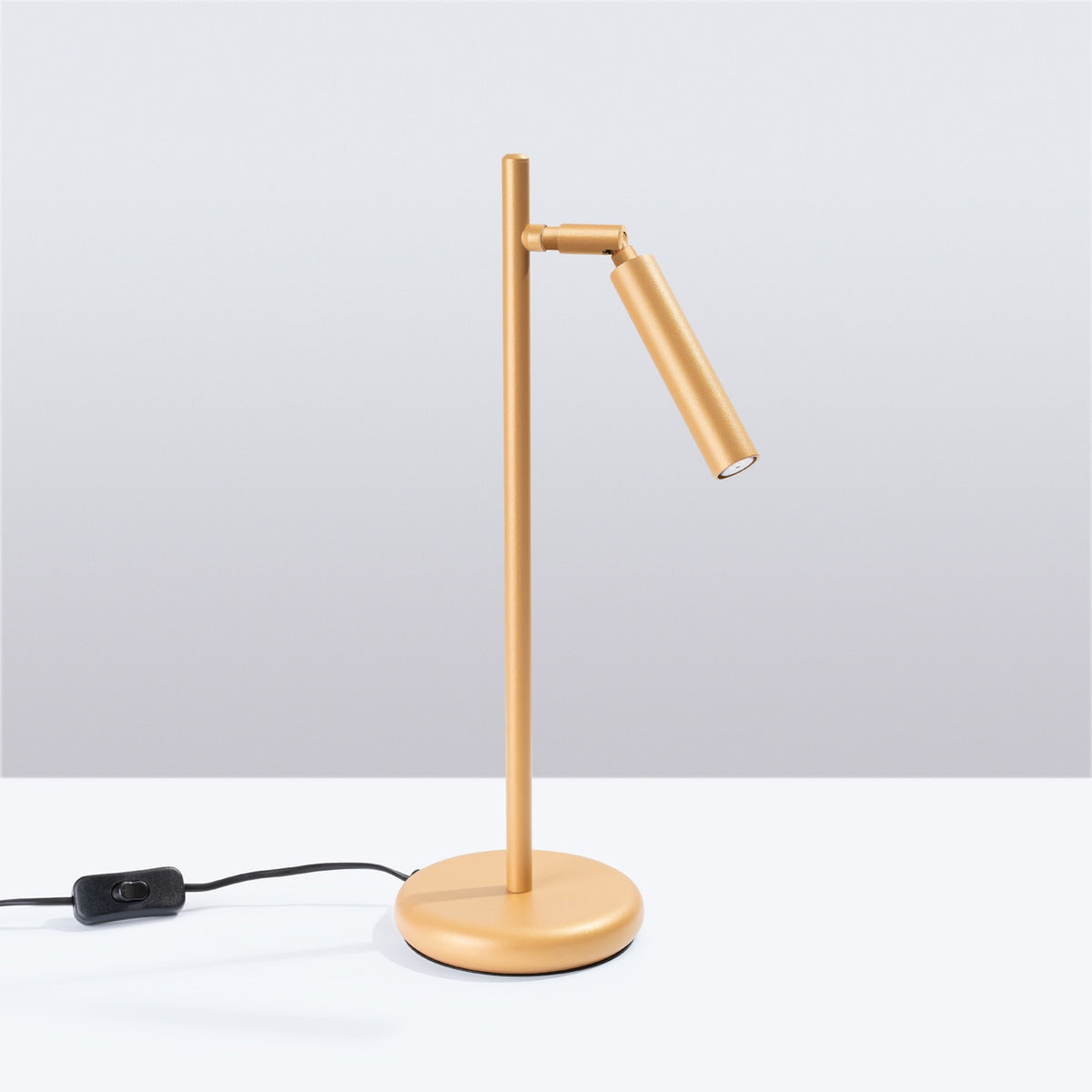 Vue de face de la lampe dorée posée sur un plan blanc.
