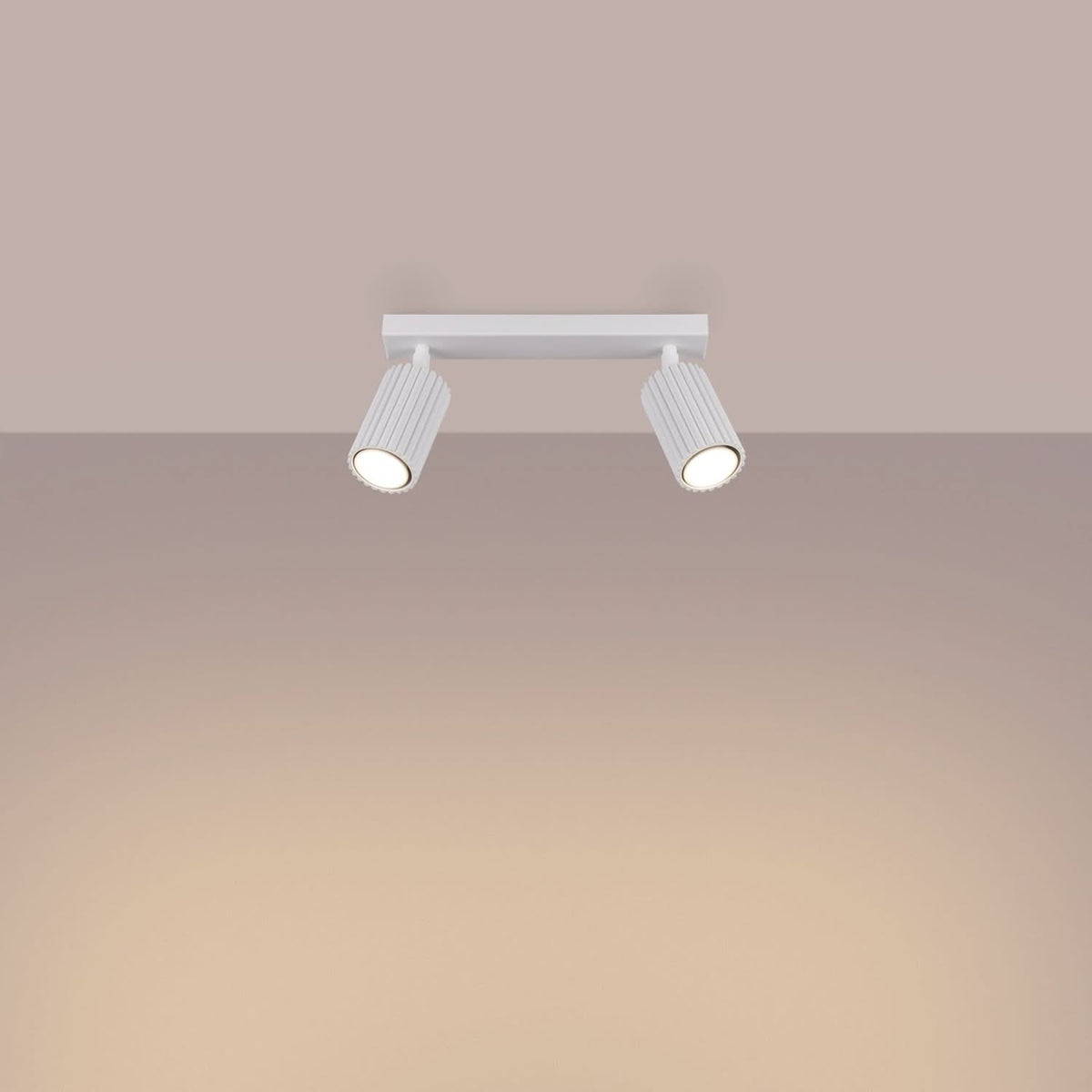 Mise en ambiance du plafonnier allumé, faisceaux chauds projetés sur un mur beige