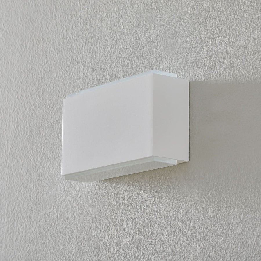 Vue de face de l'applique blanche éteinte, fixée sur un mur crème texturé.