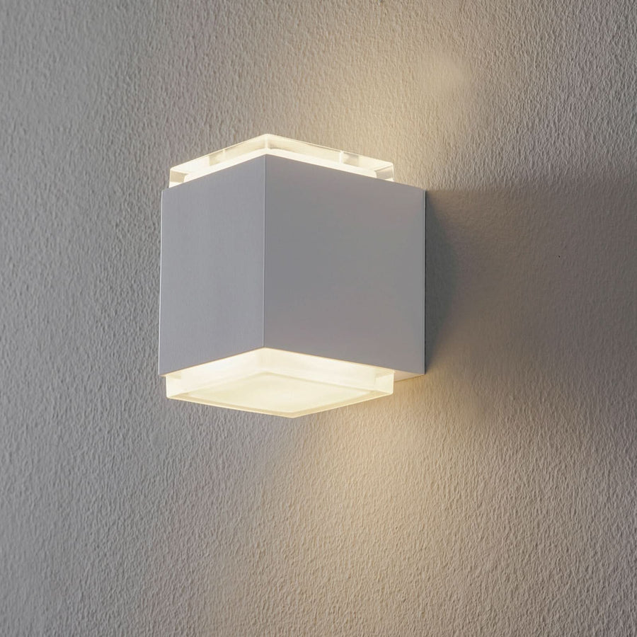 Applique murale cubique blanche allumée, diffusant une lumière chaude vers le haut et le bas.