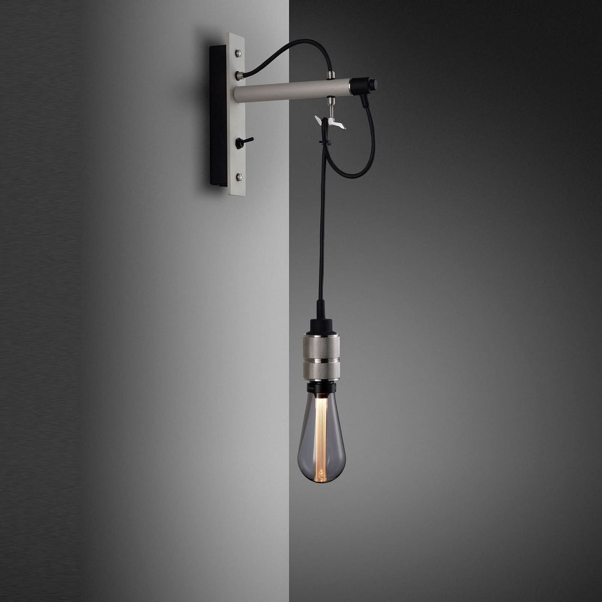 Vue rapprochée de l’applique grise fixée au mur, câble noir et douille métallique visibles.