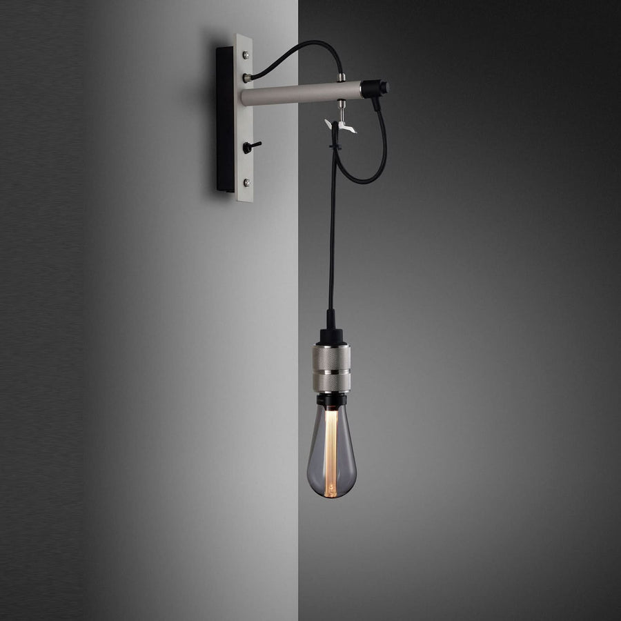 Vue rapprochée de l’applique grise fixée au mur, câble noir et douille métallique visibles.