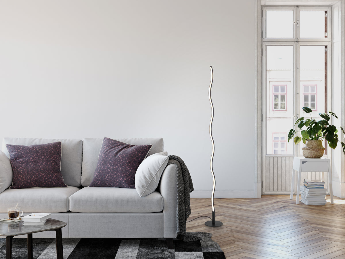 Mise en ambiance dans un salon clair, lampadaire noir ondulé près du canapé et fenêtre.