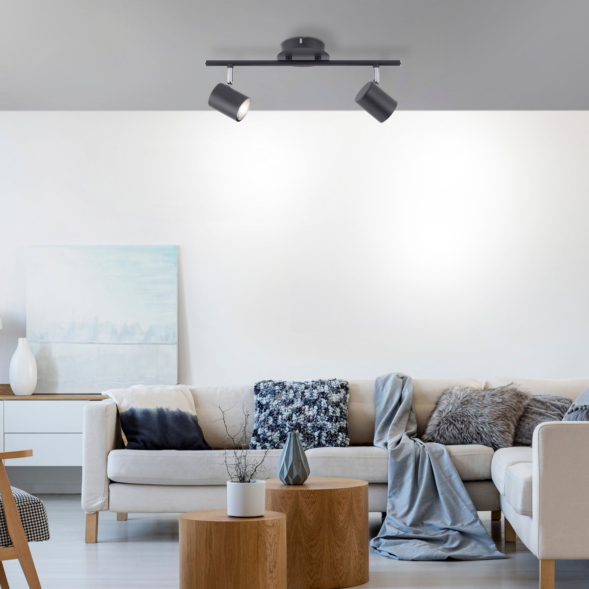 Mise en ambiance dans un salon, plafonnier anthracite éclairant un mur blanc