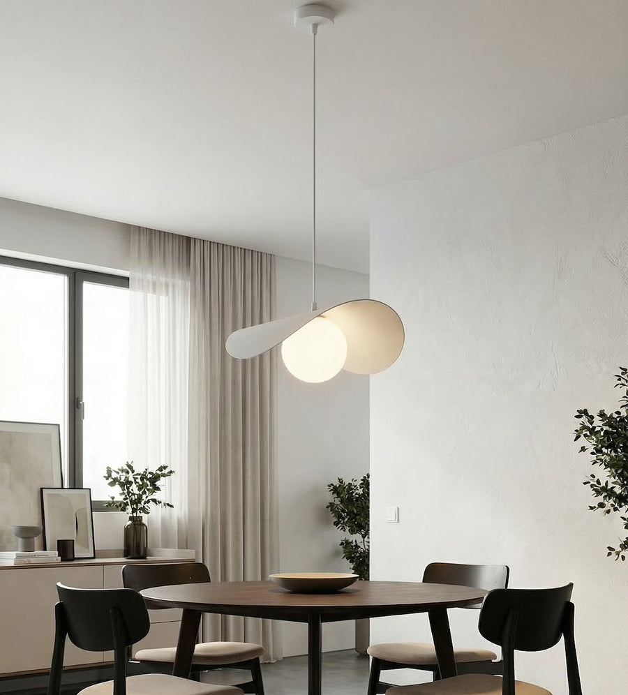 Suspension blanche éclairant une salle à manger, table ronde en bois et chaises sombres.