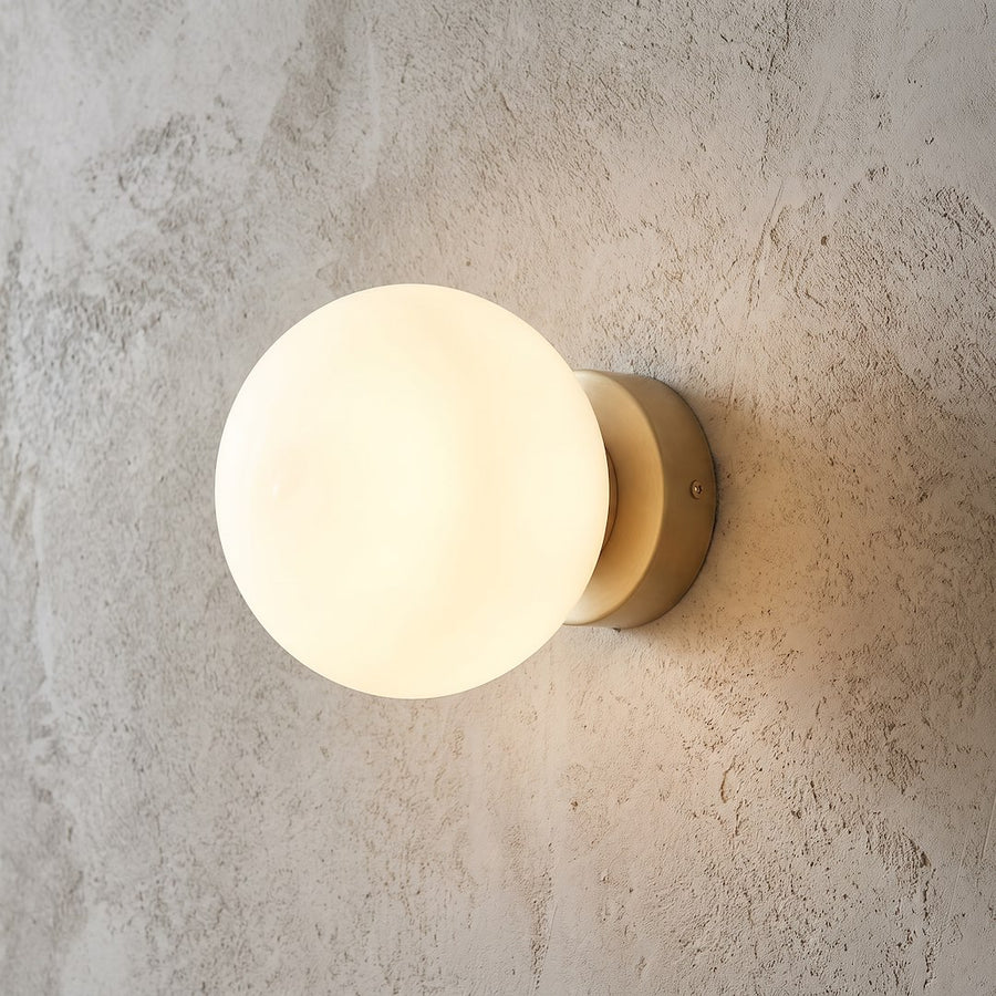 Détail de la finition : globe opalin allumé et base métallique beige sur mur brut