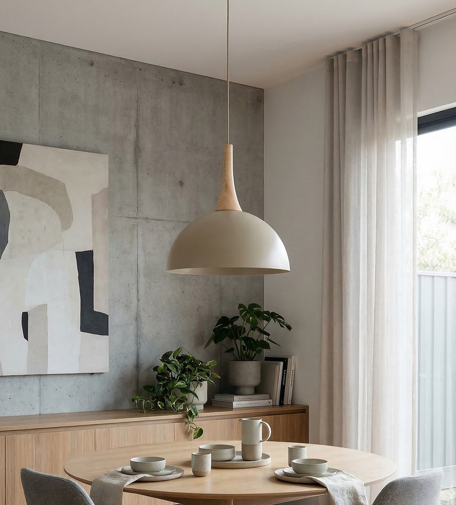 Suspension allumée dans une salle à manger, mur béton et table en bois clair