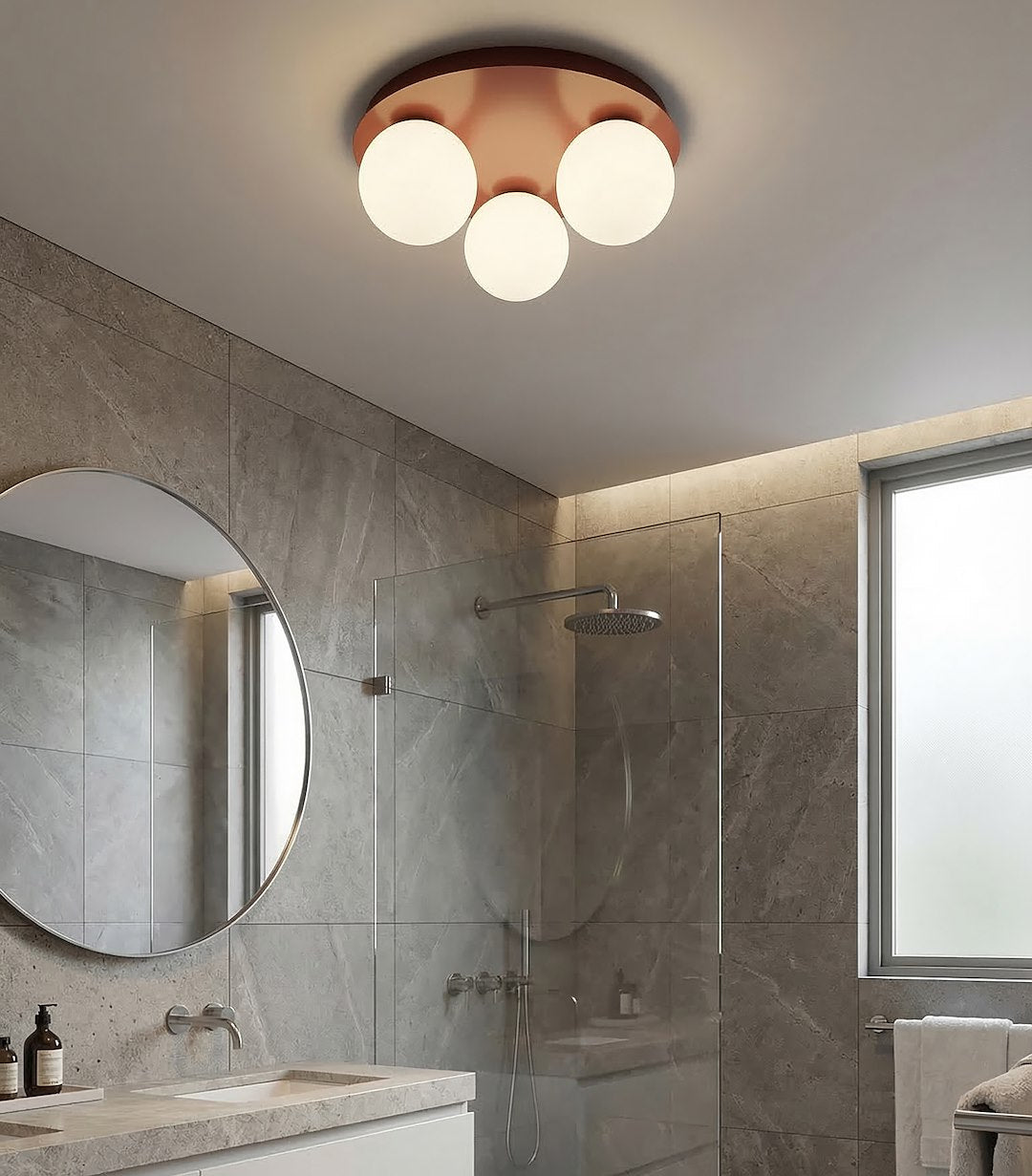 Ambiance salle de bain carrelée grise, plafonnier allumé au-dessus du miroir rond