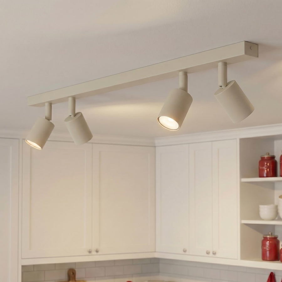 Plafonnier beige fixé au plafond d'une cuisine, quatre spots allumés éclairent les meubles blancs.