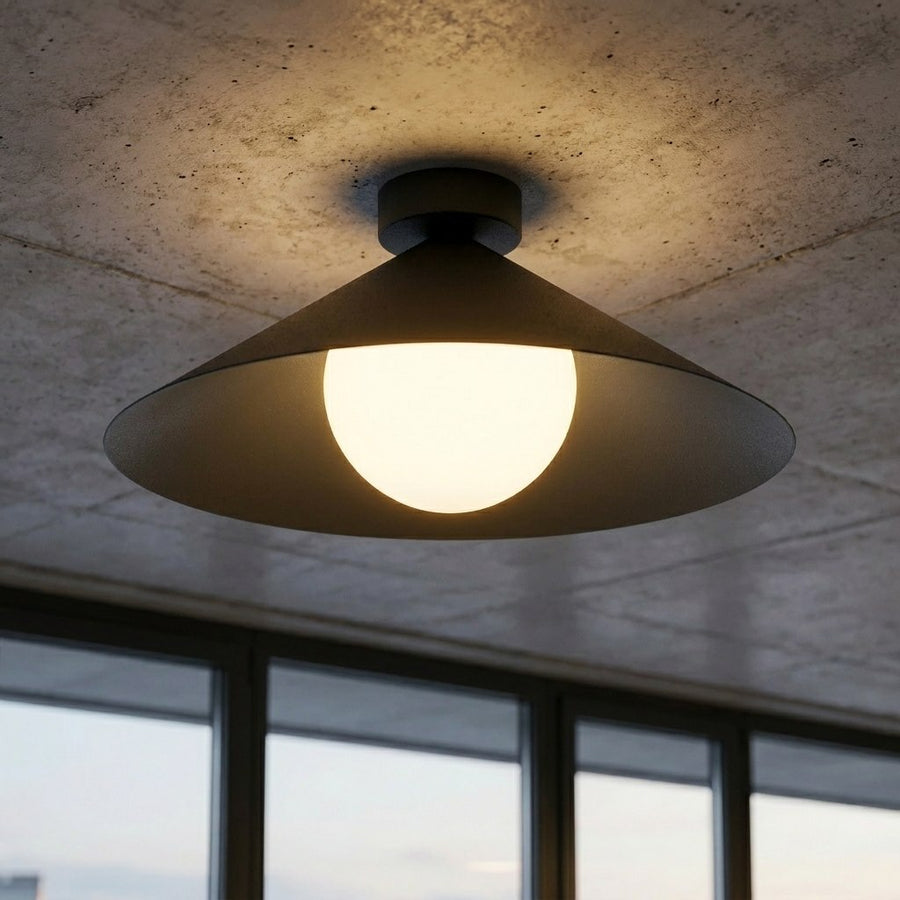 Gros plan sur le diffuseur en verre allumé, fixé sous un plafond béton brut.