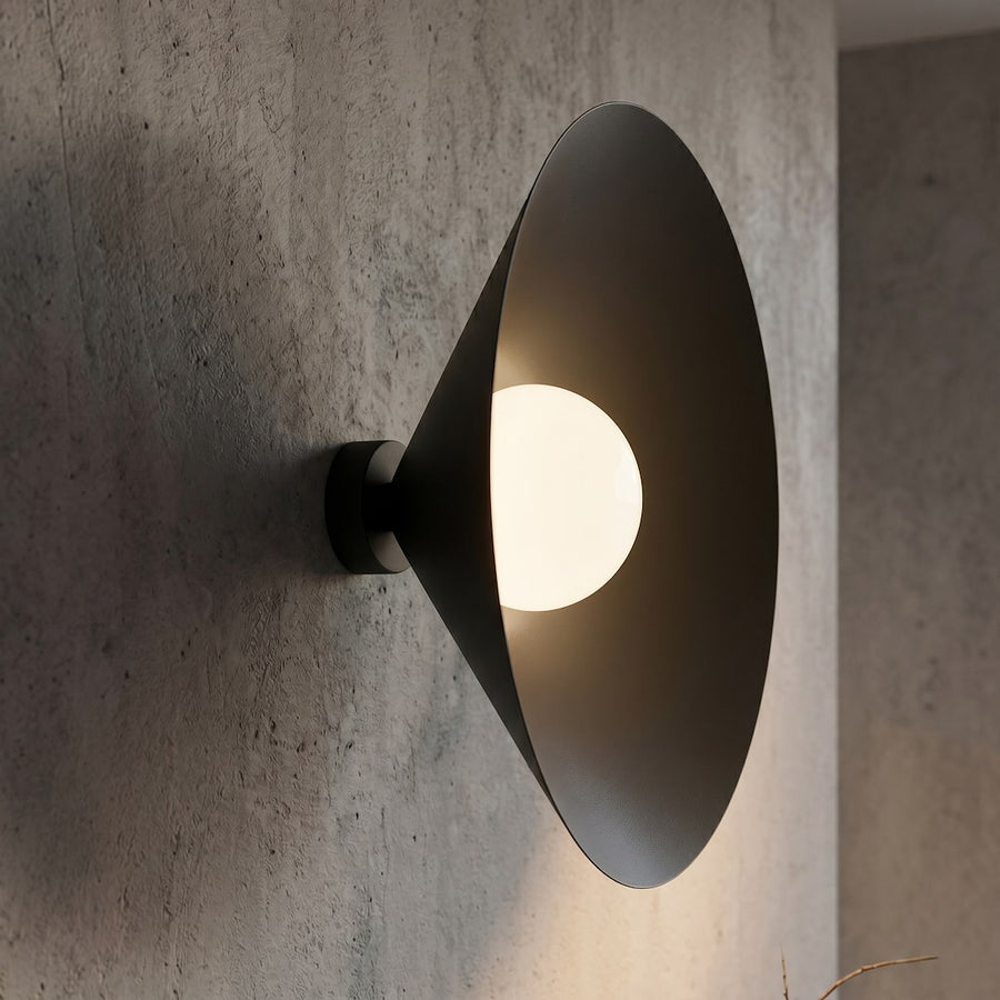 Applique allumée sur béton brut, halo lumineux chaud autour du globe