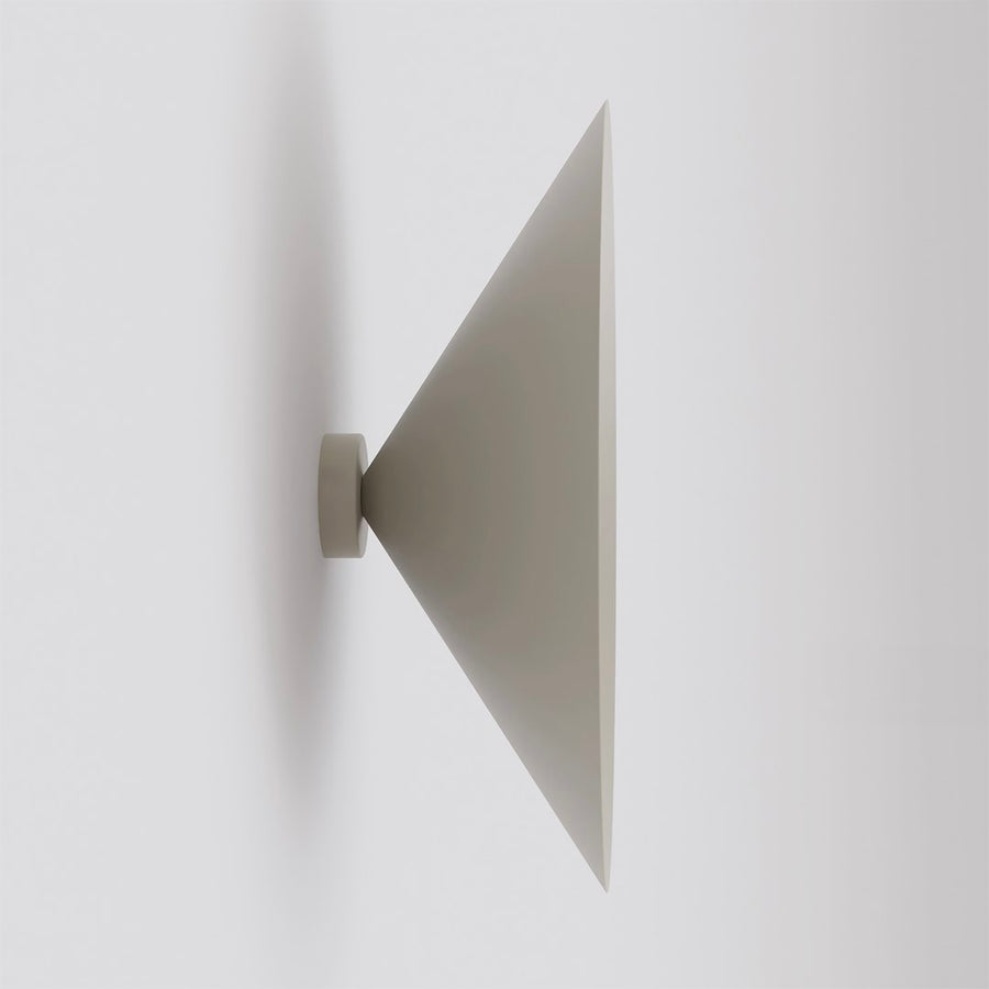 Vue de profil d'une applique murale beige en forme de cône sur mur blanc.