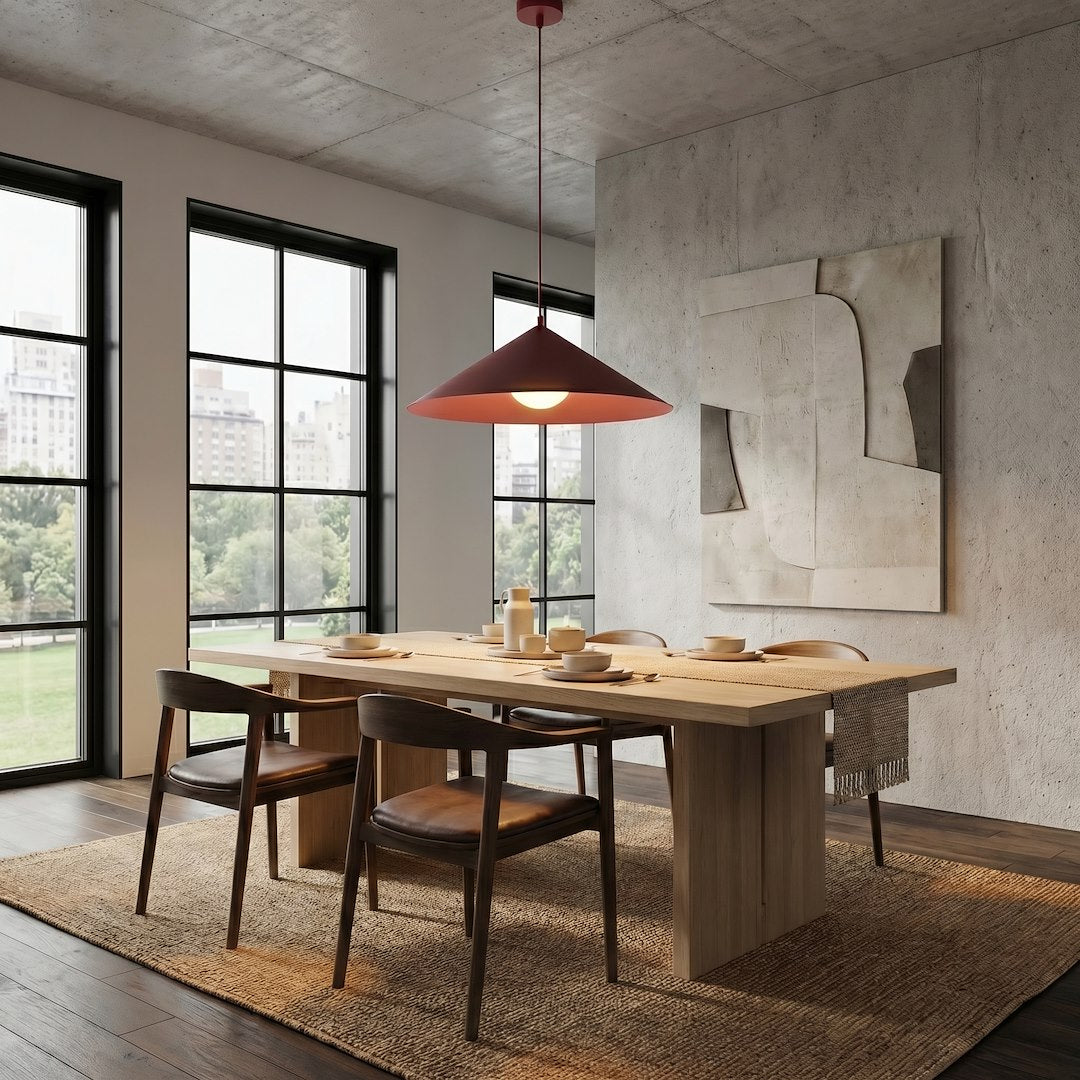 Pièce en béton avec grande table dressée, suspension bordeaux éclairée vue de loin