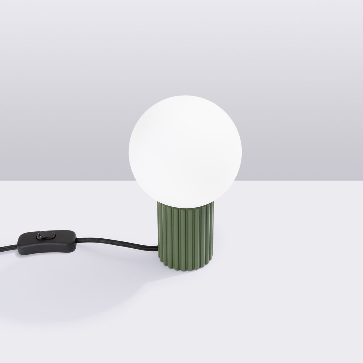 Vue de face de la lampe verte avec interrupteur noir en ligne sur le cordon tressé.