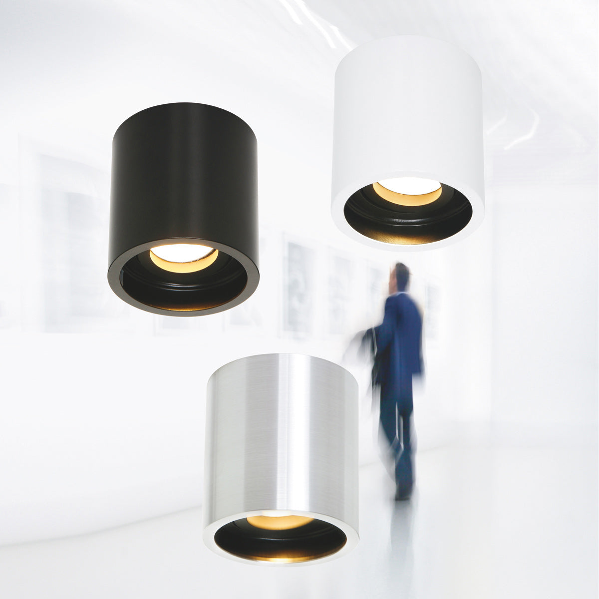 Trois spots cylindriques noir, blanc et argent présentés en ambiance galerie