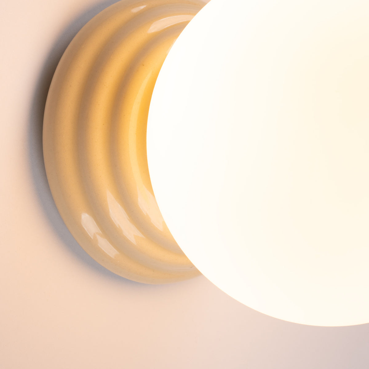 Gros plan sur la base céramique beige et le globe blanc, éclairage chaud.