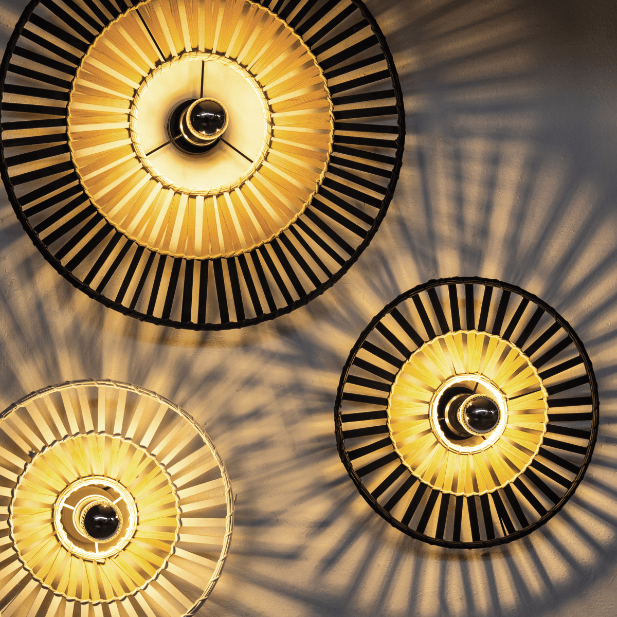 Vue rapprochée de trois luminaires allumés, détail des cercles concentriques et des ombres portées.