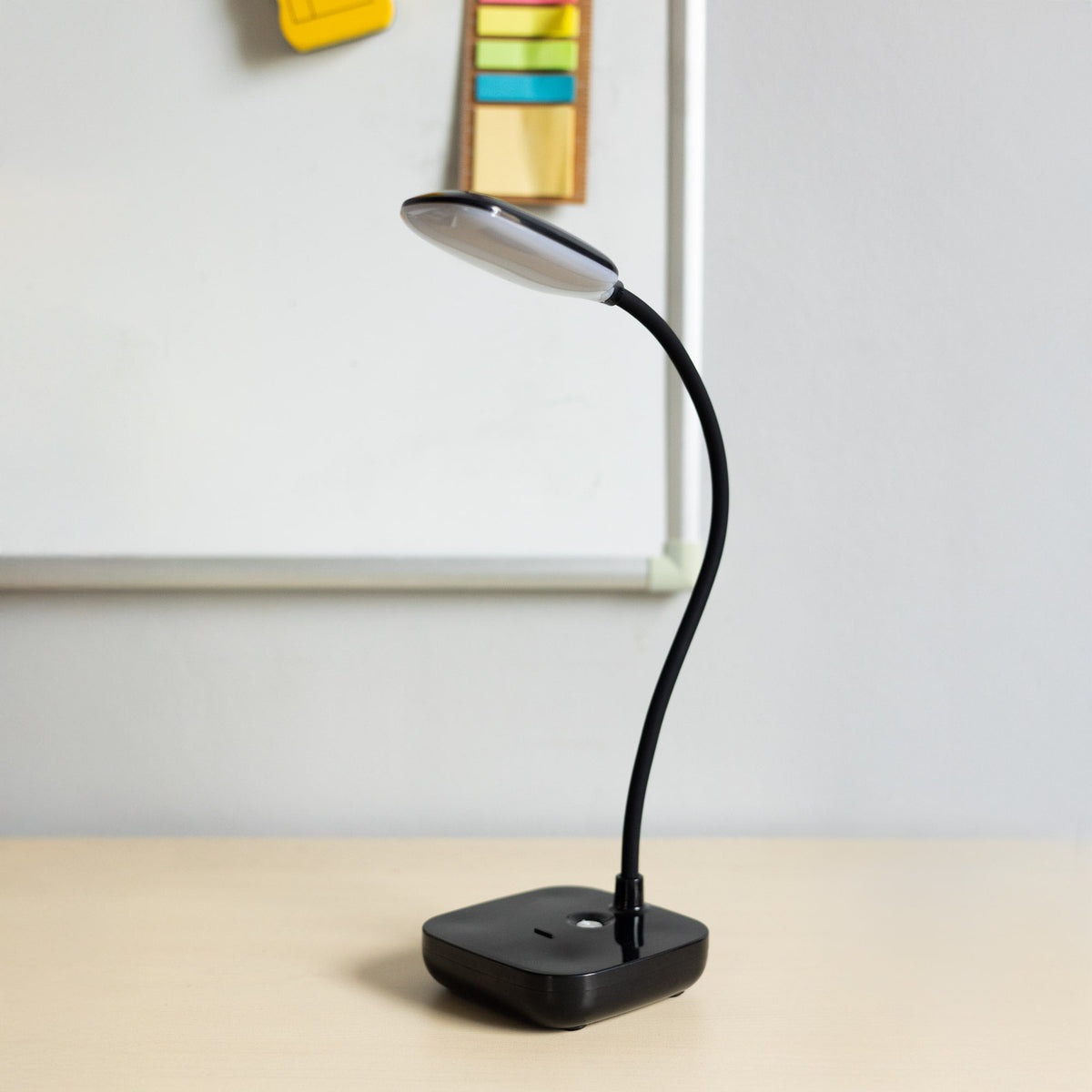 Lampe posée sur un bureau clair devant un tableau blanc et des notes colorées.