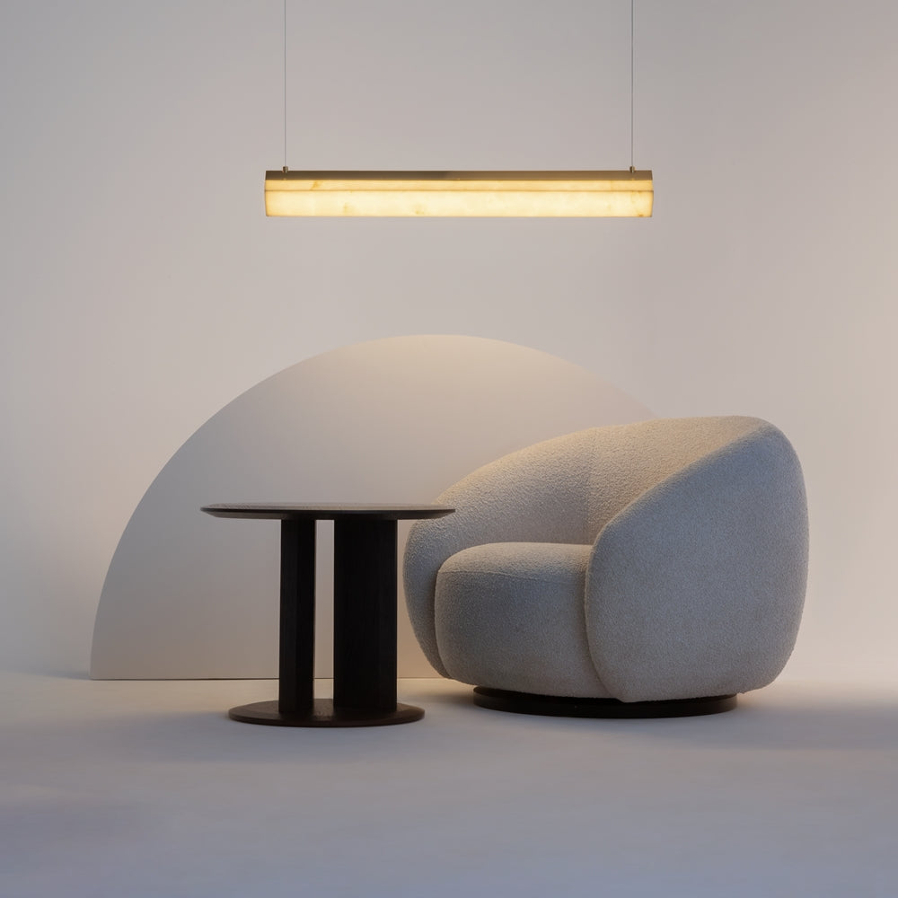 Mise en ambiance avec luminaire suspendu au-dessus d'une table noire et fauteuil gris.