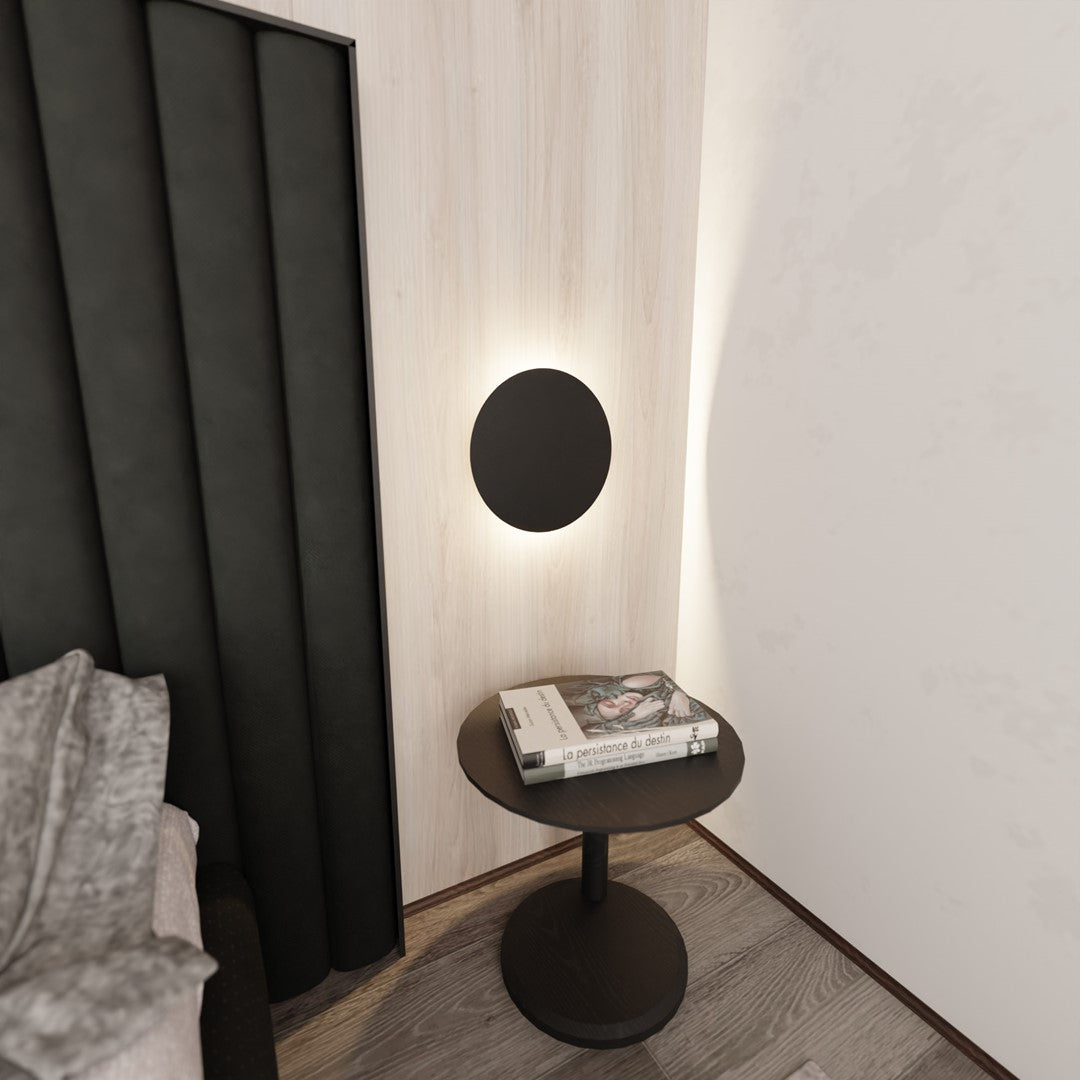 Vue de biais avec table d'appoint noire et lit, éclairage mural indirect.