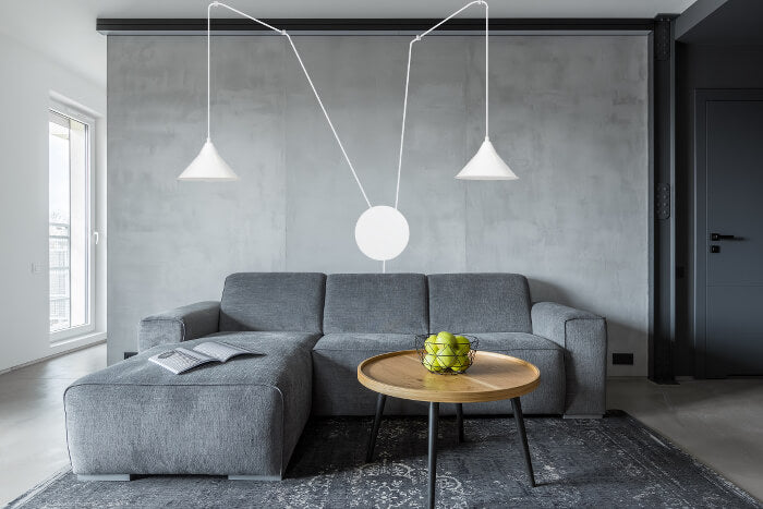 Ambiance intérieure béton gris, canapé d'angle et table ronde sous la suspension double.