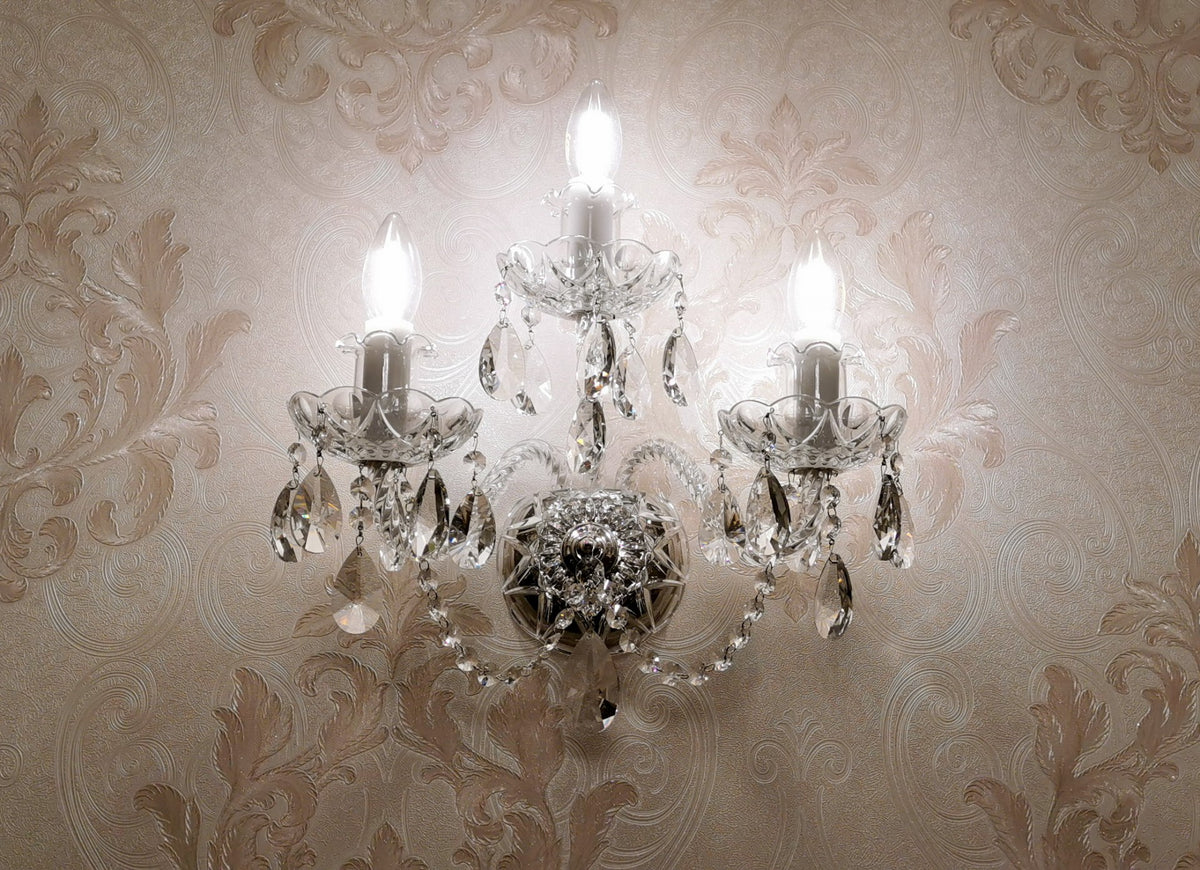 Applique en cristal allumée, installée sur un mur à papier peint damassé beige