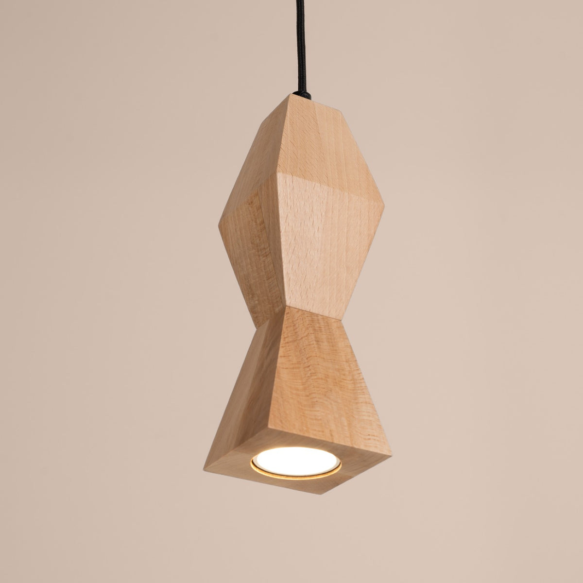 Plan rapproché du luminaire suspendu allumé, abat-jour en bois facetté et câble noir
