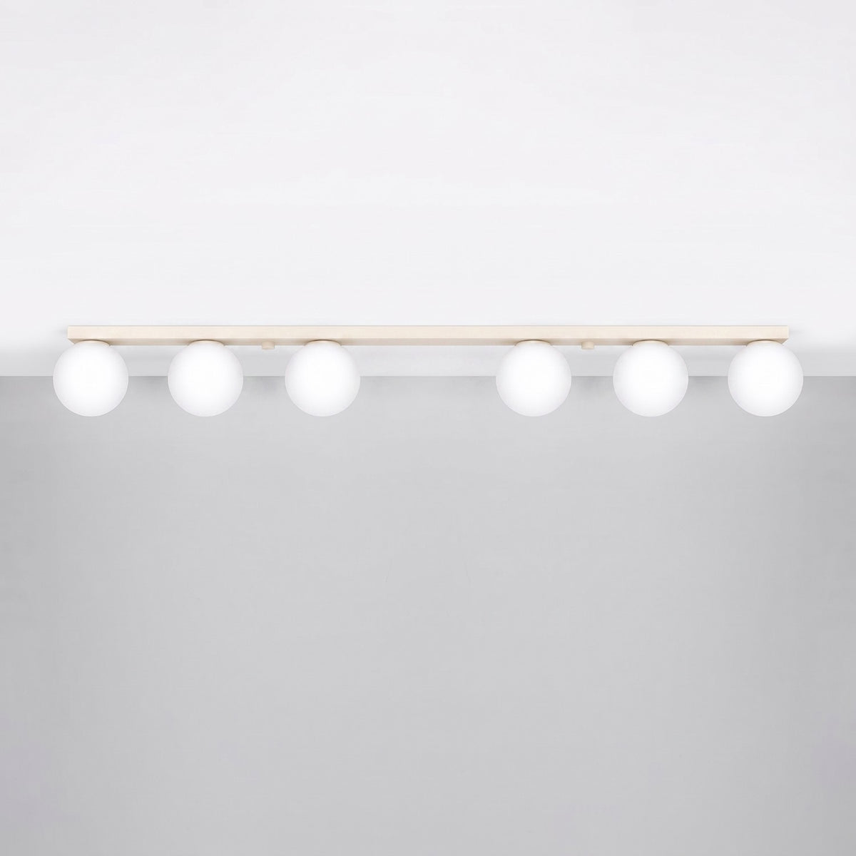 Luminaire installé au plafond, six globes blancs suspendus sous une barre beige.