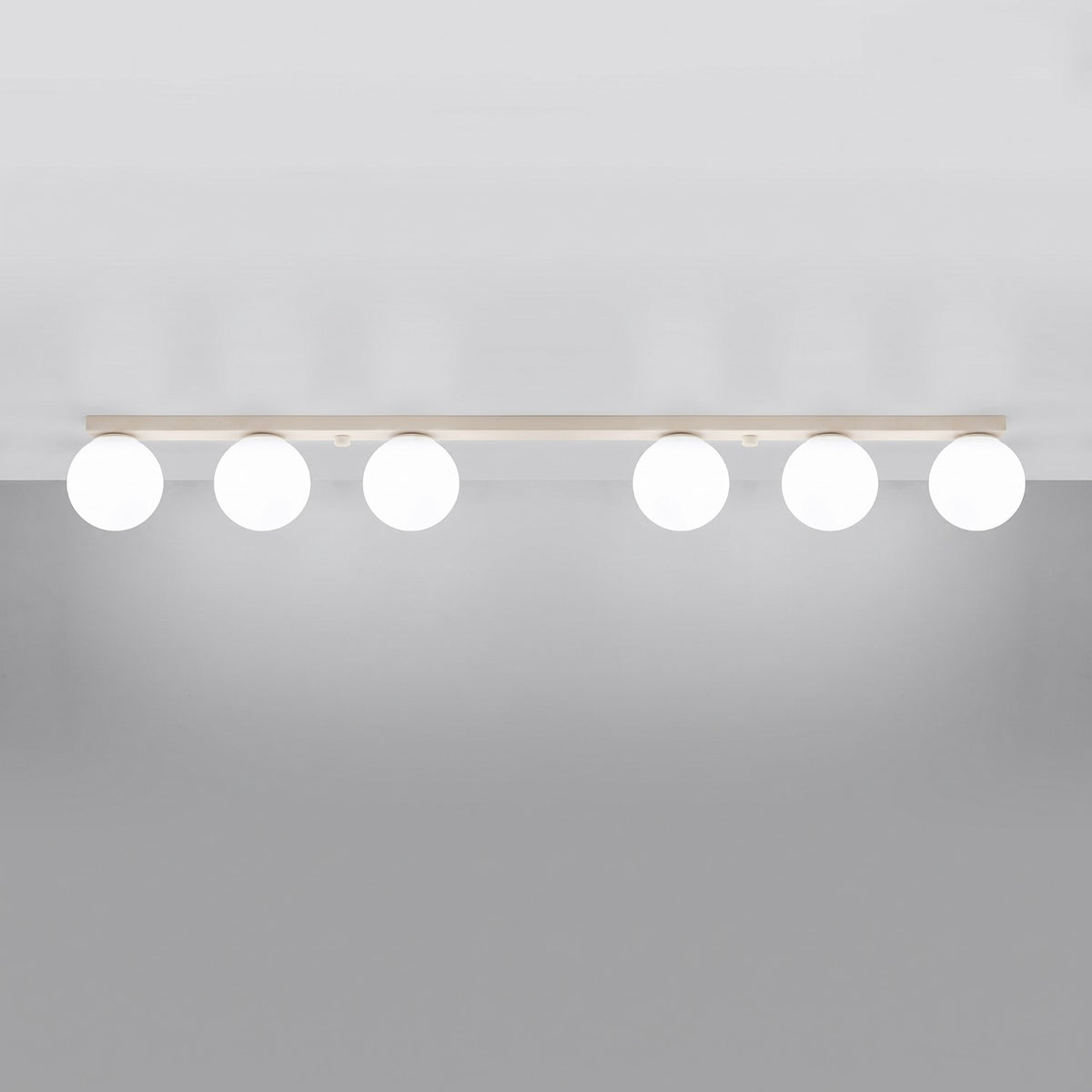 Plafonnier allumé au plafond, six globes diffusent une lumière douce sur fond gris.