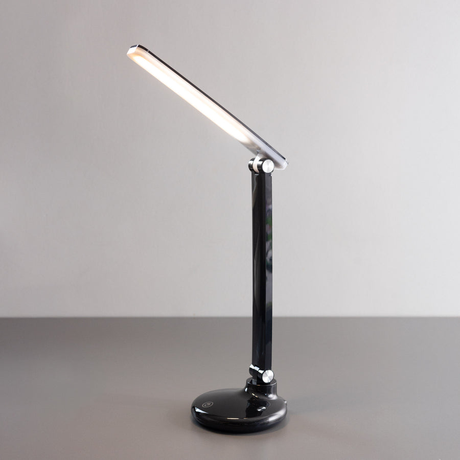 Lampe de bureau noire vue de face, tête inclinée allumée sur fond clair