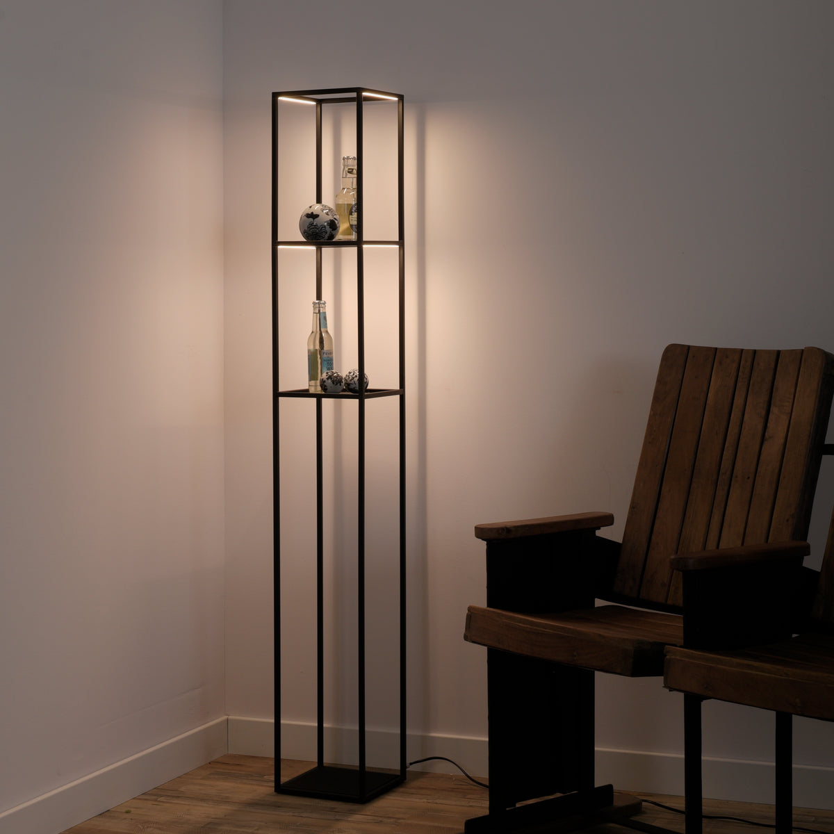 Mise en ambiance dans un coin avec fauteuil en bois, étagères éclairées et objets décoratifs.