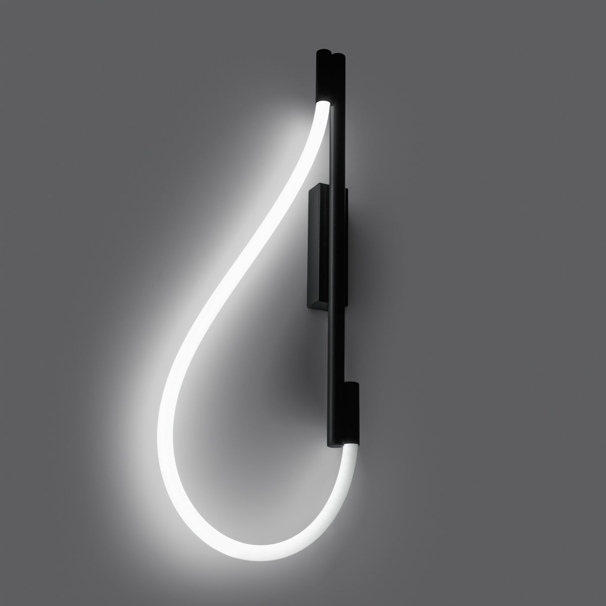 Applique allumée sur mur gris foncé, halo lumineux diffus autour de la boucle.