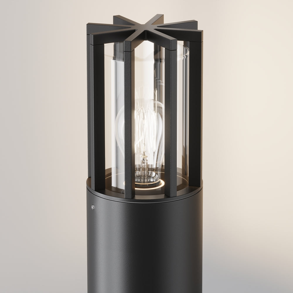 Détail du luminaire noir, cage métallique étoilée et ampoule filament visible sous verre.