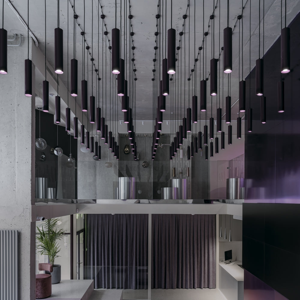 Mise en ambiance de nombreux pendants cylindriques noirs suspendus à différentes hauteurs dans un intérieur