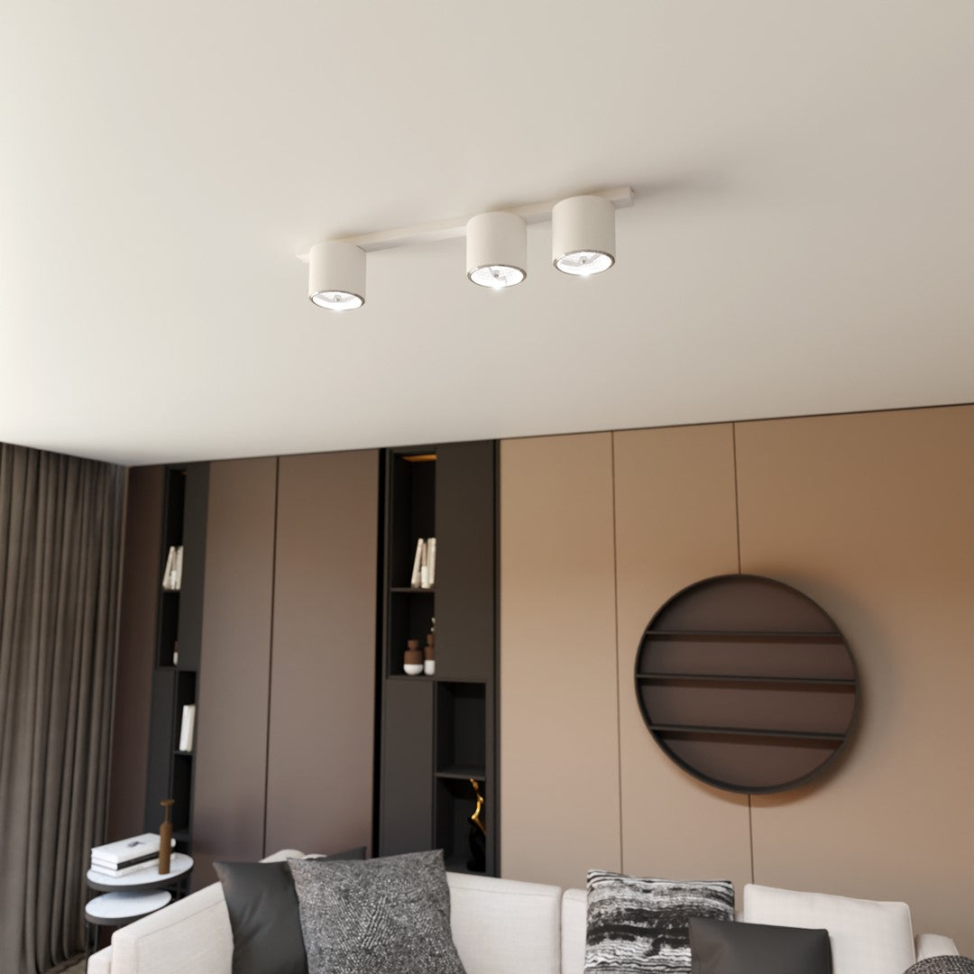 Luminaire blanc trois spots installé au plafond dans un salon moderne meublé.