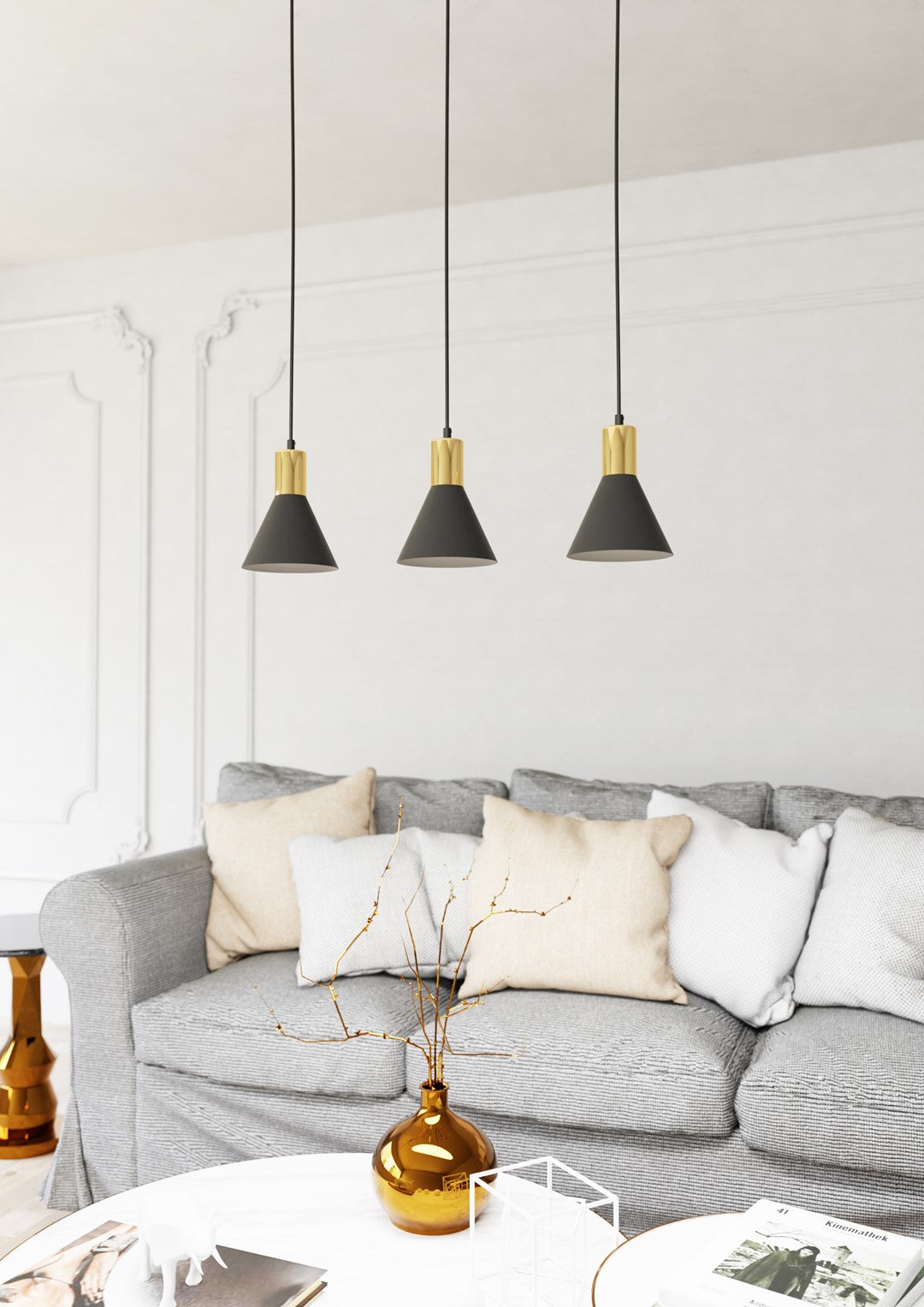 Suspension trois lumières éclairant un salon devant un canapé gris et moulures blanches
