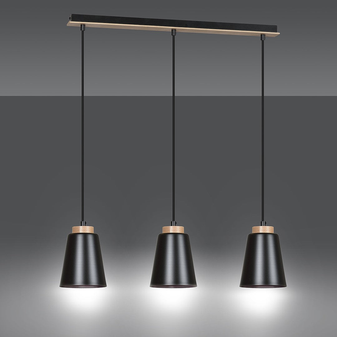 Suspension allumée sur fond gris, les trois abat-jours noirs diffusent une lumière chaude.