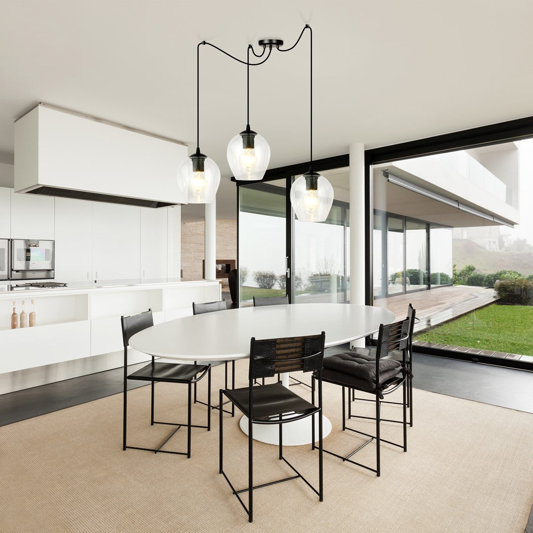Mise en ambiance : trois suspensions allumées au-dessus d'une table ovale, cuisine blanche lumineuse