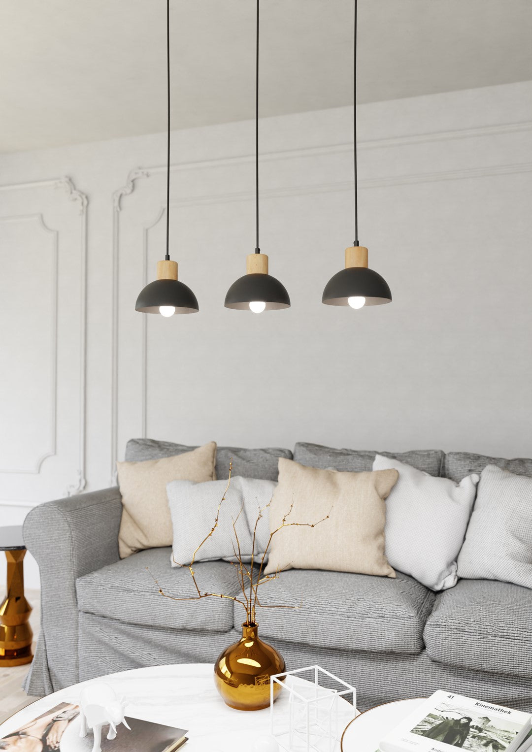 Ambiance salon : trois suspensions noires au-dessus d'un canapé gris et coussins.
