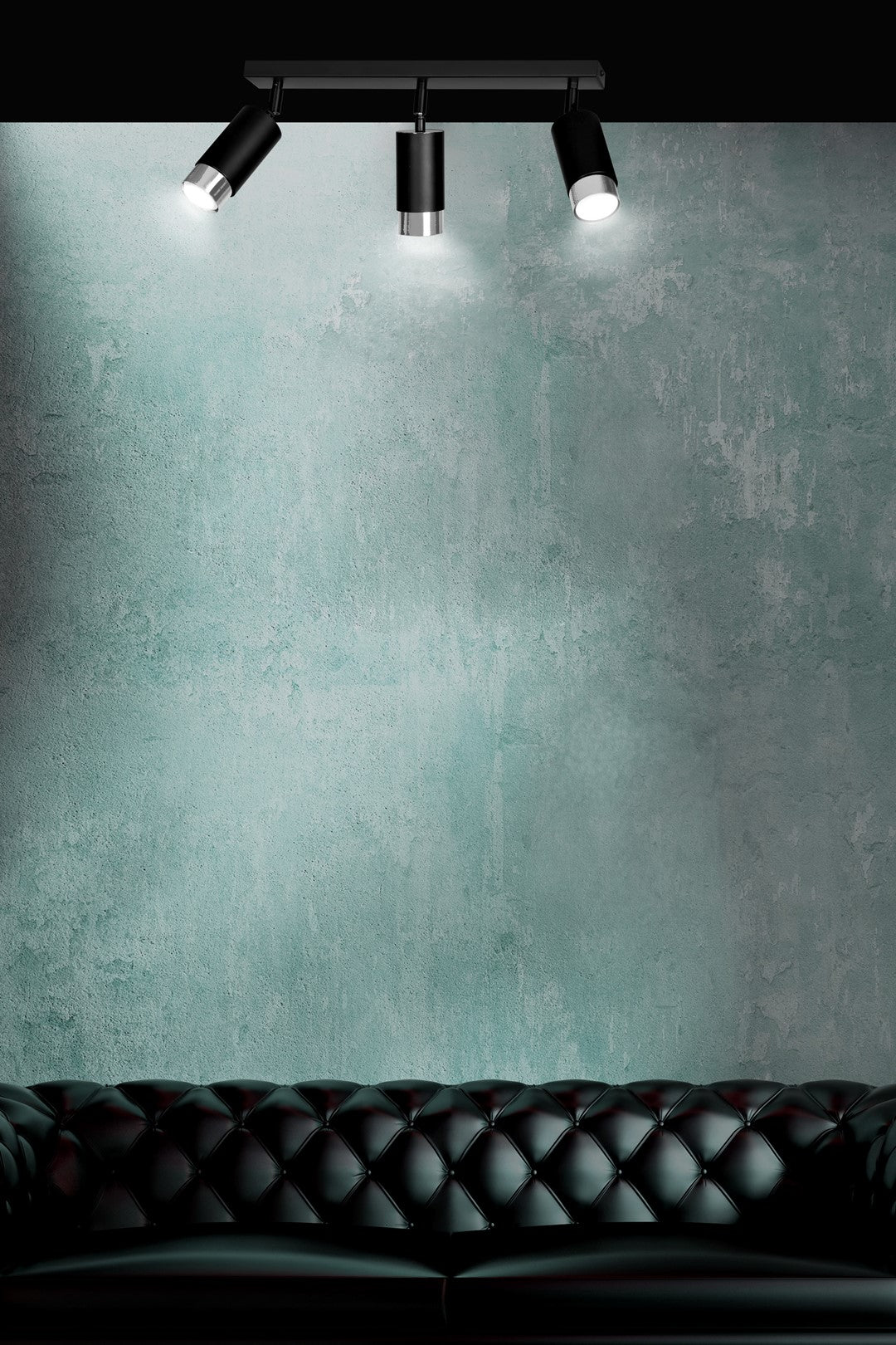 Mise en ambiance au-dessus d'un canapé en cuir noir, mur vert béton fortement éclairé.